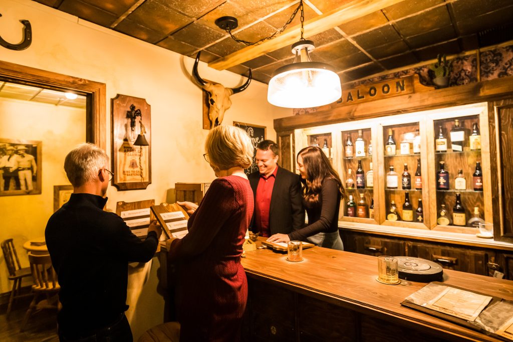 Équipe en activité dans un décor de saloon western chez Défi-Évasion, résolvant une énigme autour d’un bar en bois